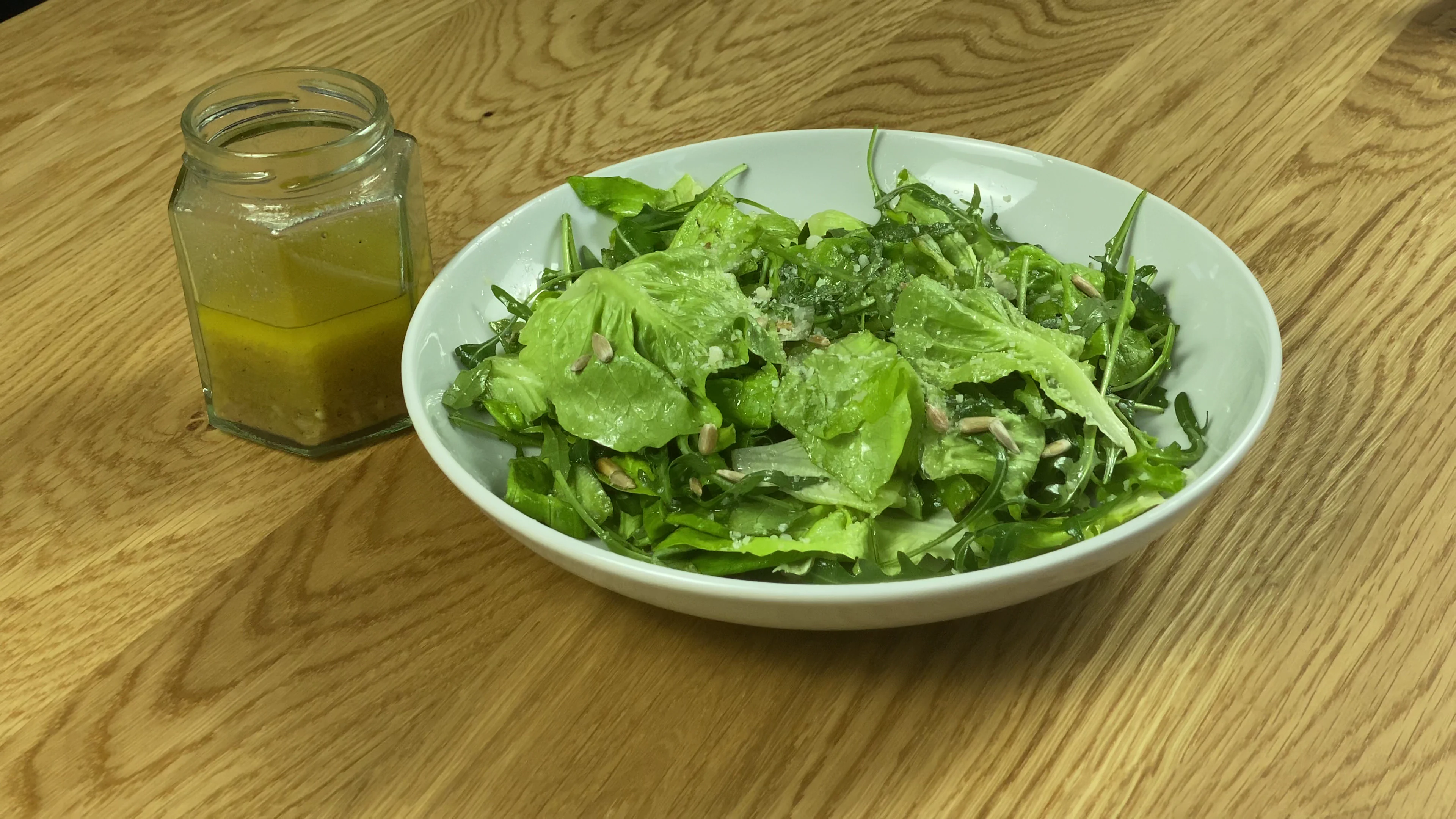 A fresh green salad in a white bowl with a small jar of creamy dressing on the side.