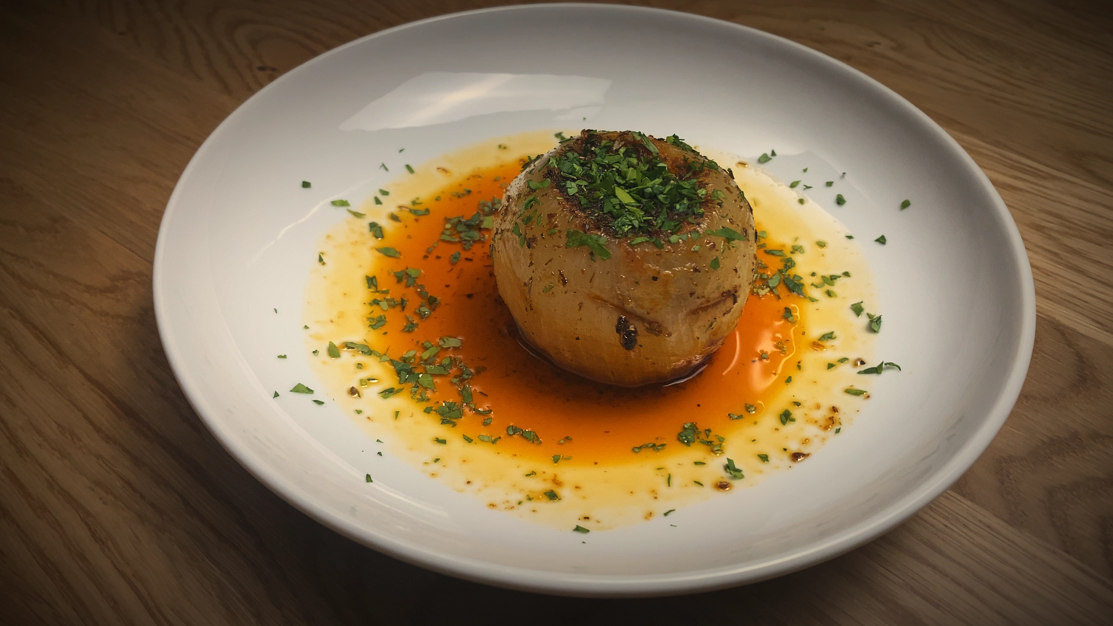 Viral onion boil style whole onion on a shallow white plate, garnished with chopped parsley and sitting in a pool of melted butter, olive oil, Cajun seasoning, crushed fennel seeds, and lemon juice.