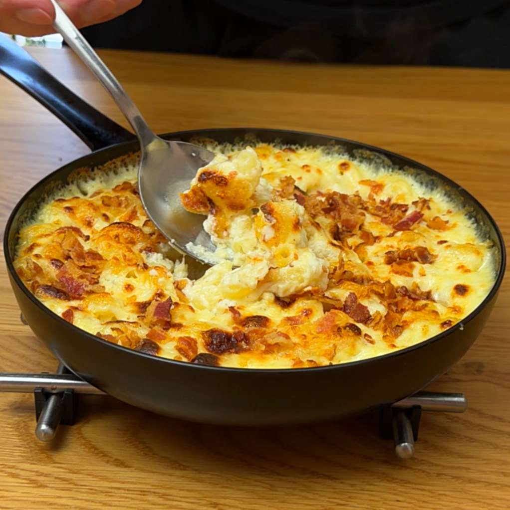 Spoon scooping creamy mac and cheese with bacon from a pan