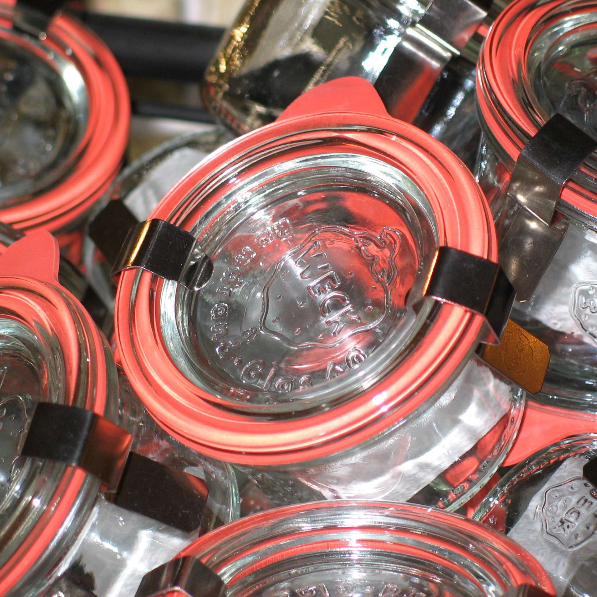 Close-up of glass Weck canning jars with orange rubber rings and metal clamps.