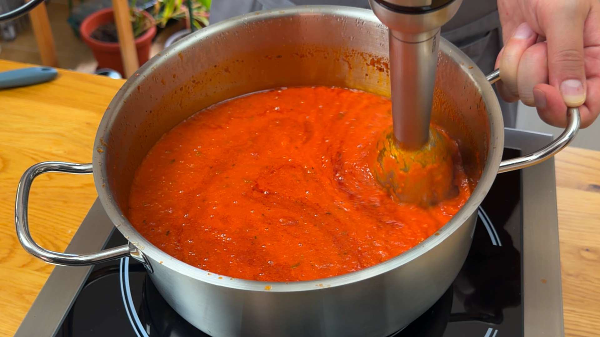 Using an immersion hand blender to purée red tomato marinara sauce in a pot on the stove.