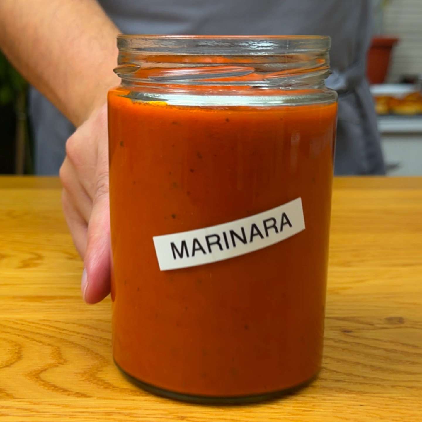A glass jar filled with smooth homemade marinara sauce labeled "MARINARA" resting on a wooden table.