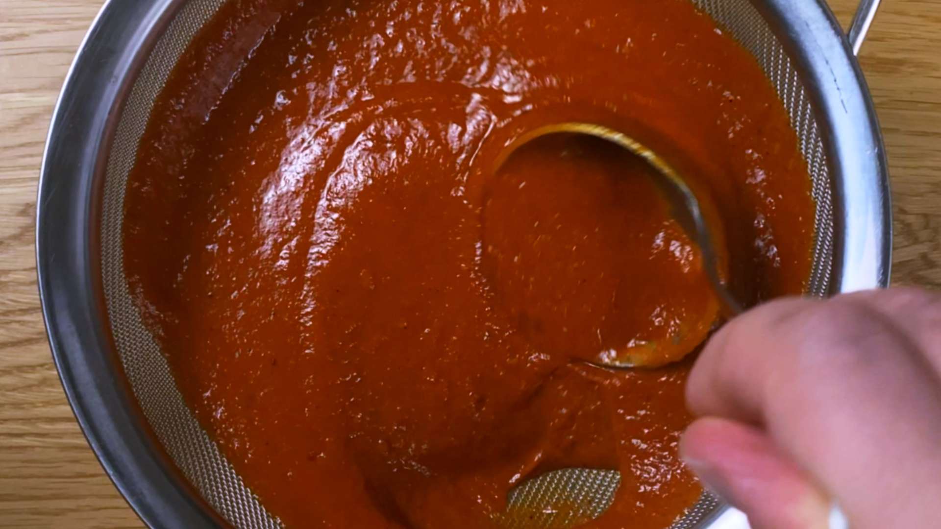 Straining smooth homemade tomato ketchup through a fine mesh sieve.