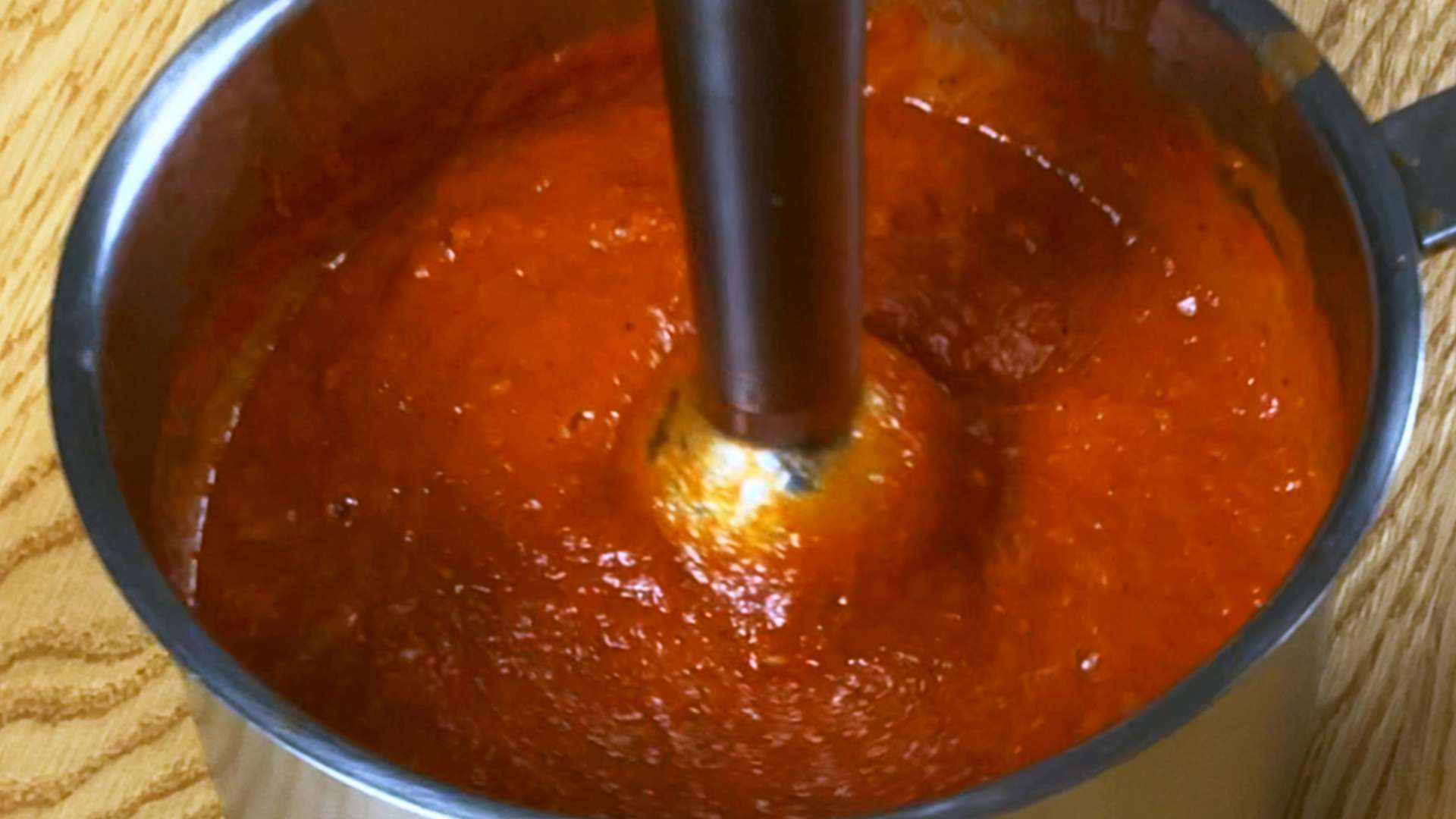 Blending cooked tomato sauce with an immersion blender for homemade ketchup.