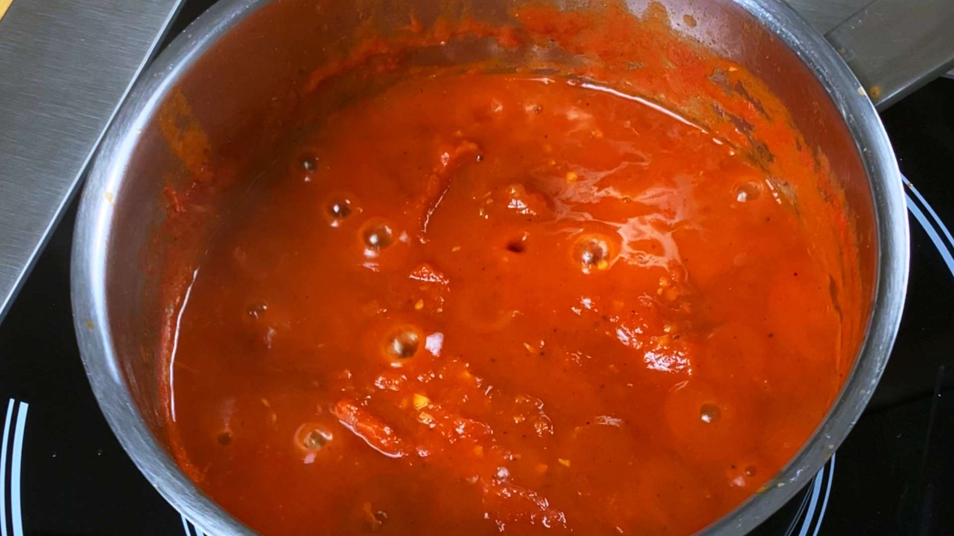 Simmering homemade tomato ketchup bubbling in a metal pot on the stove.