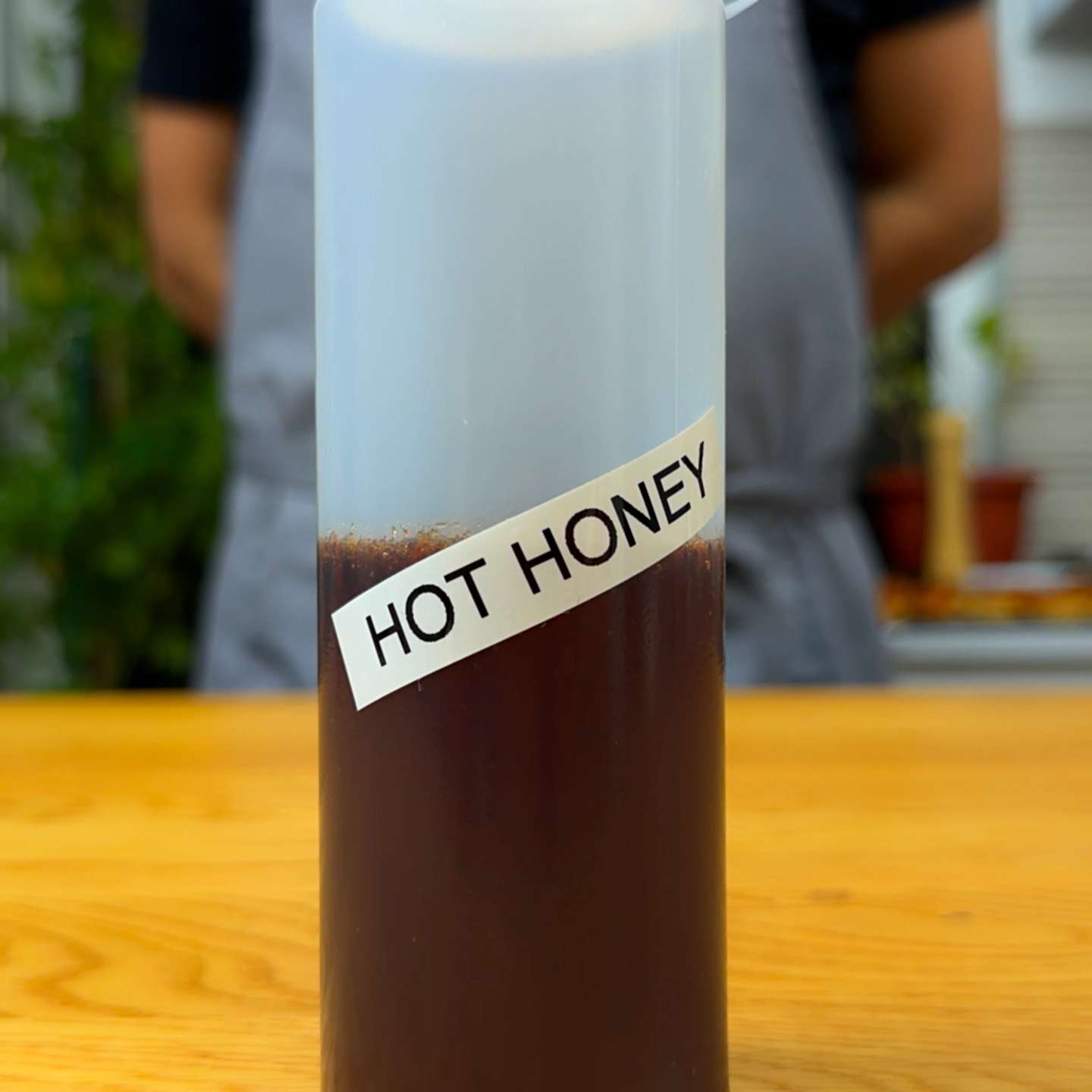 A clear plastic squeeze bottle containing dark hot honey labeled "HOT HONEY" standing on a wooden counter.