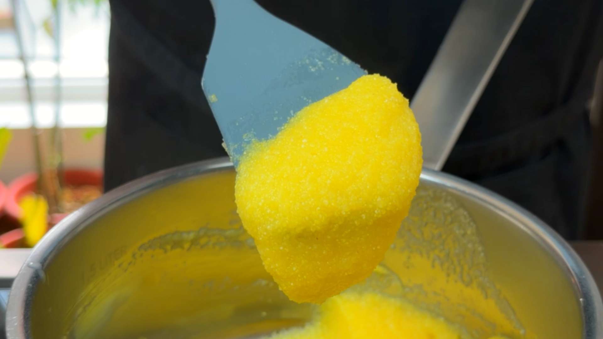 A close-up of thick, cooked instant polenta lifted on a spatula above a stainless steel pot.