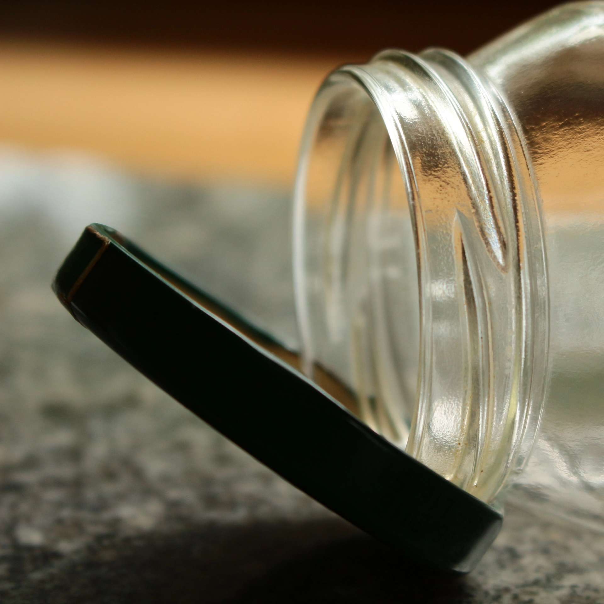 Close-up of an open, empty glass jar lying on its side next to its lid on a surface.