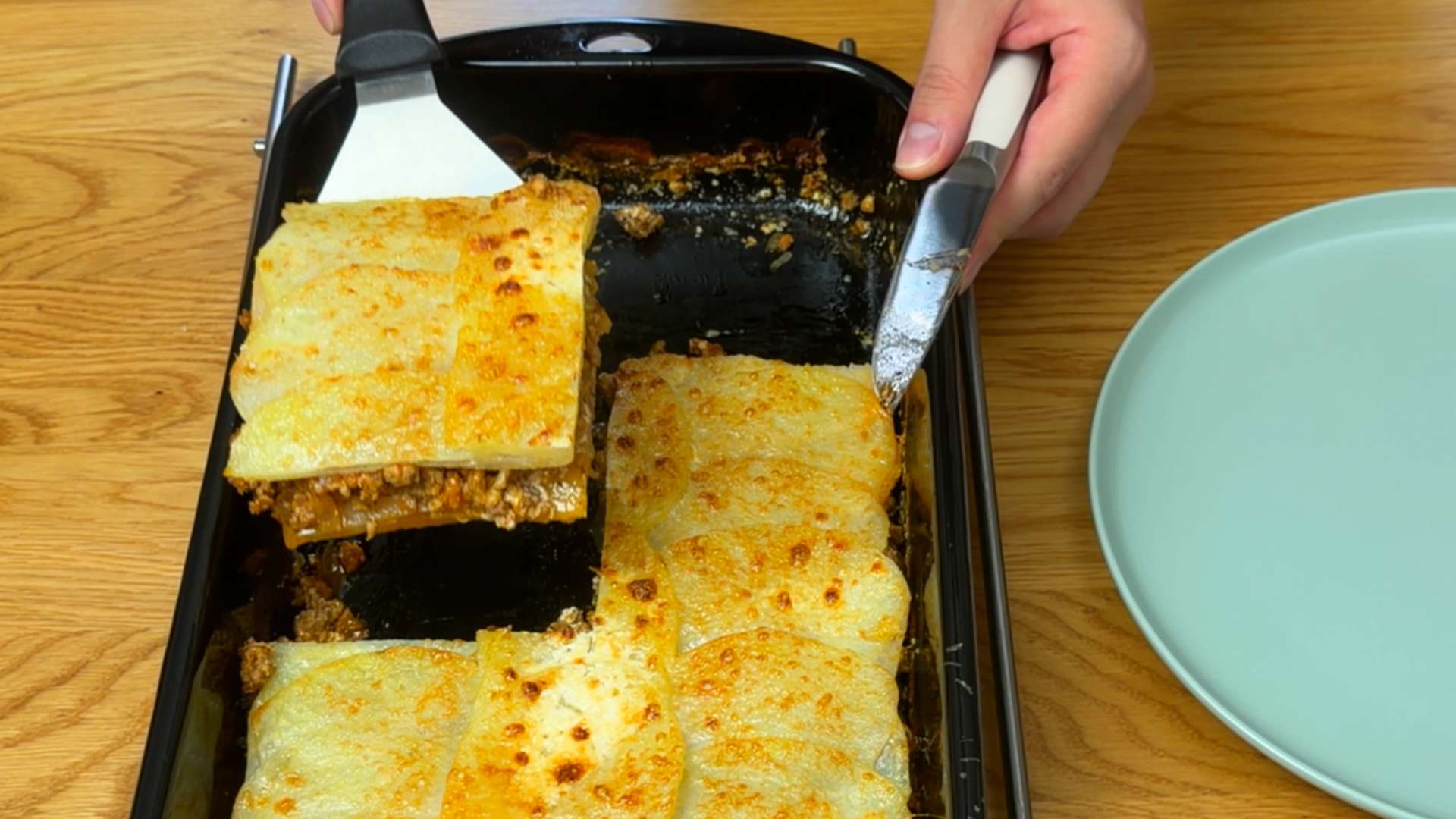 A piece of freshly baked potato moussaka with layered potatoes and minced meat being lifted from a baking pan with a spatula.