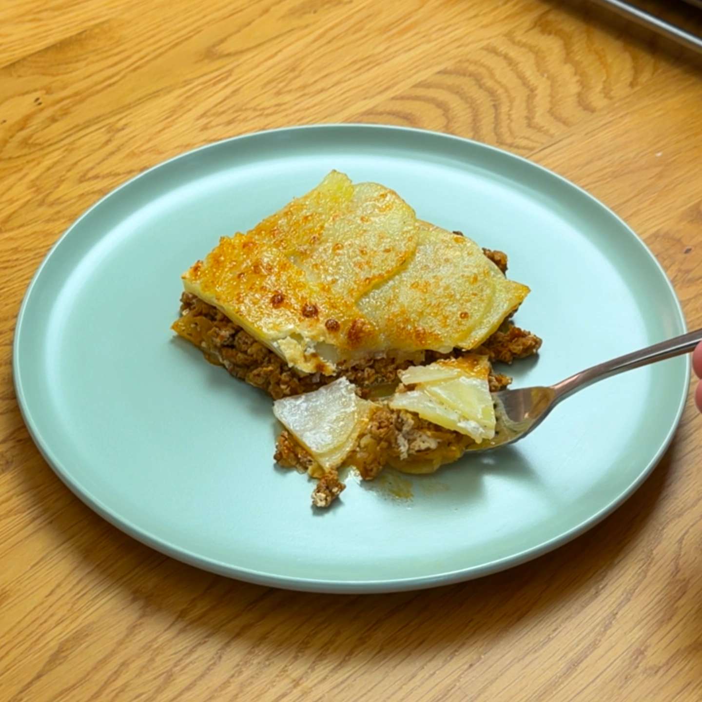 A fork taking a bite from a slice of potato moussaka on a blue plate.
