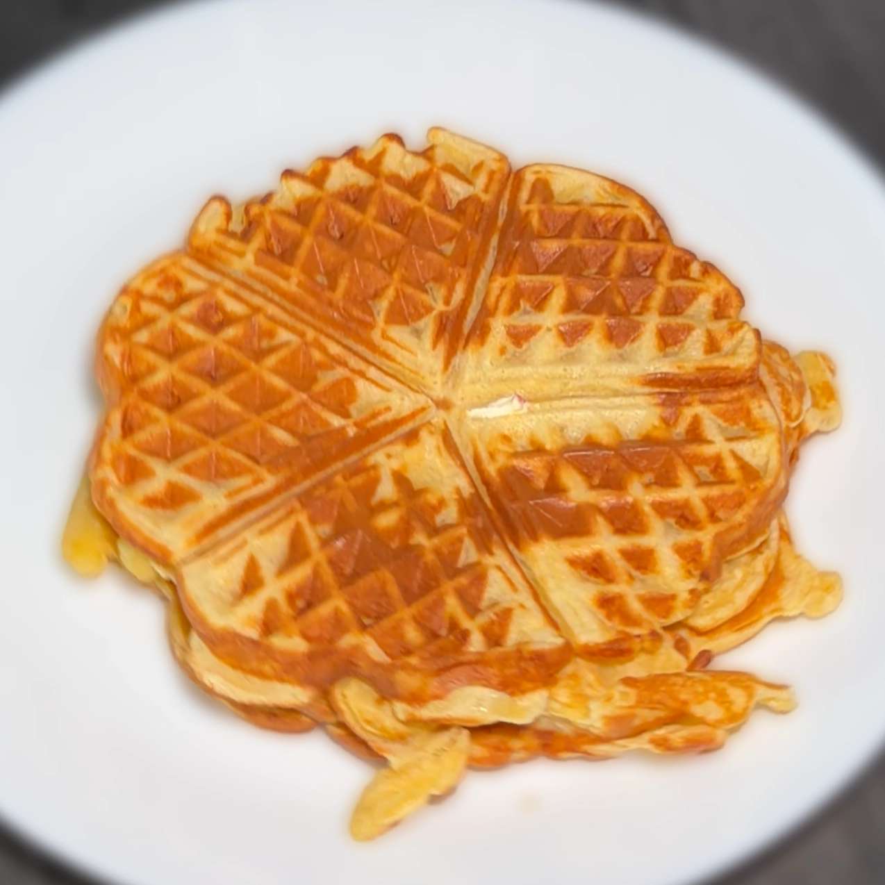 Stack of golden-brown, heart-shaped waffle sections served on a round white plate, showing a grid pattern and crisp edges.