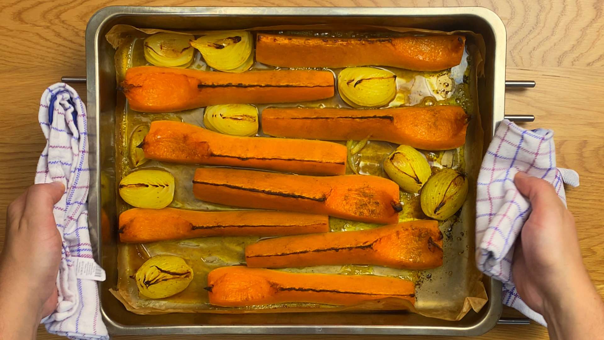 Hands holding a metal baking pan with caramelized roasted butternut squash and onion wedges.