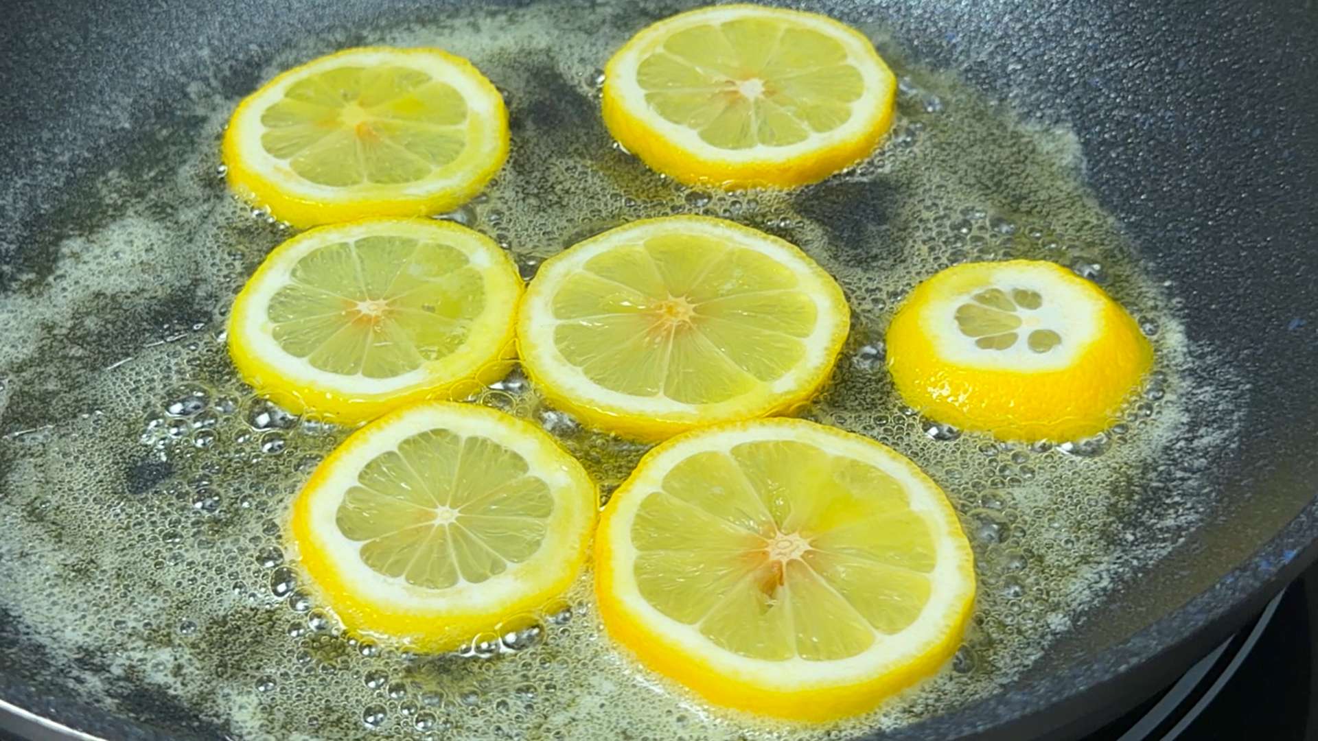 Slices of fresh lemon simmering in melted butter inside a black skillet.