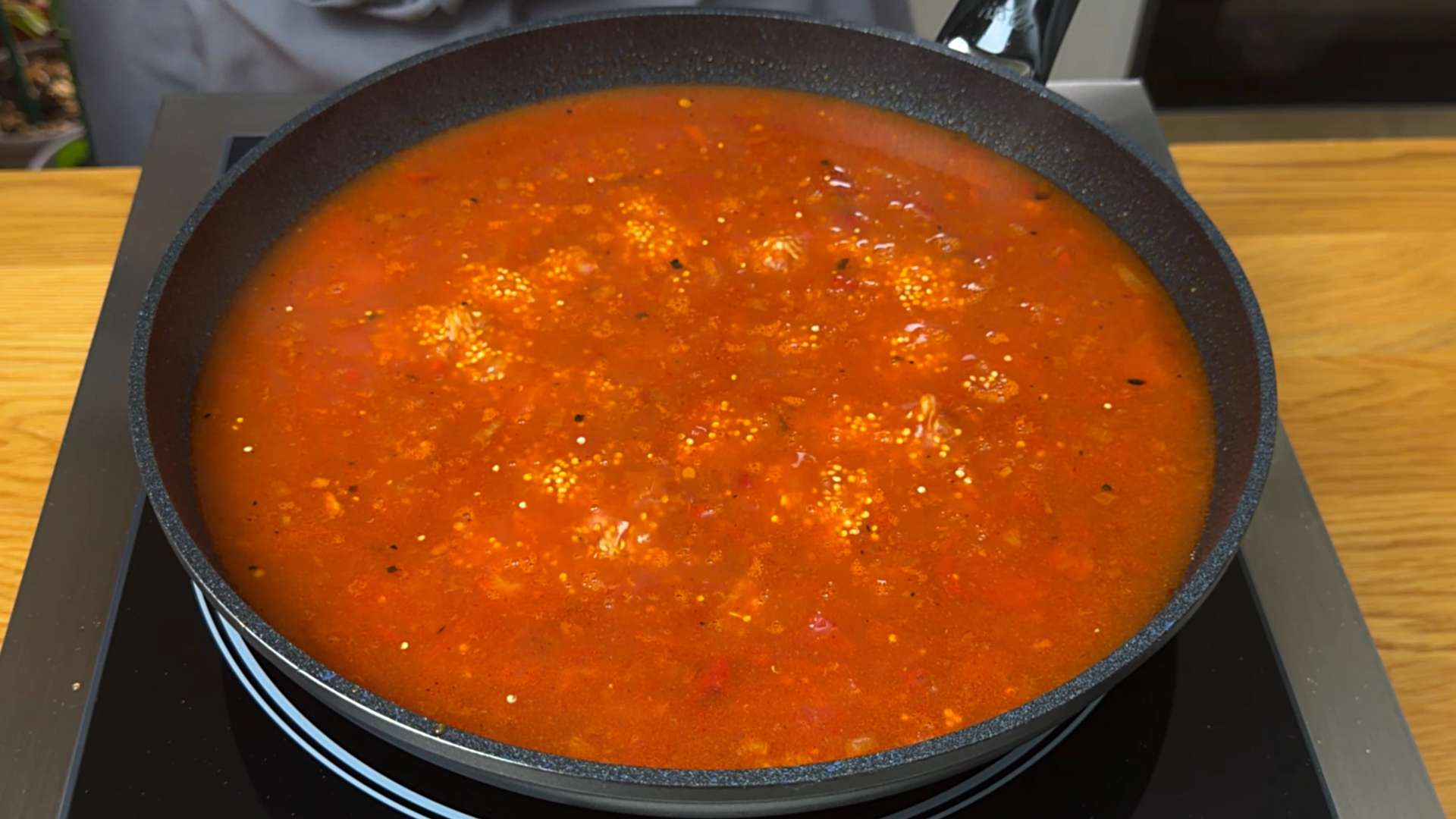 Quinoa simmering in a rich tomato and broth sauce inside a black pan.
