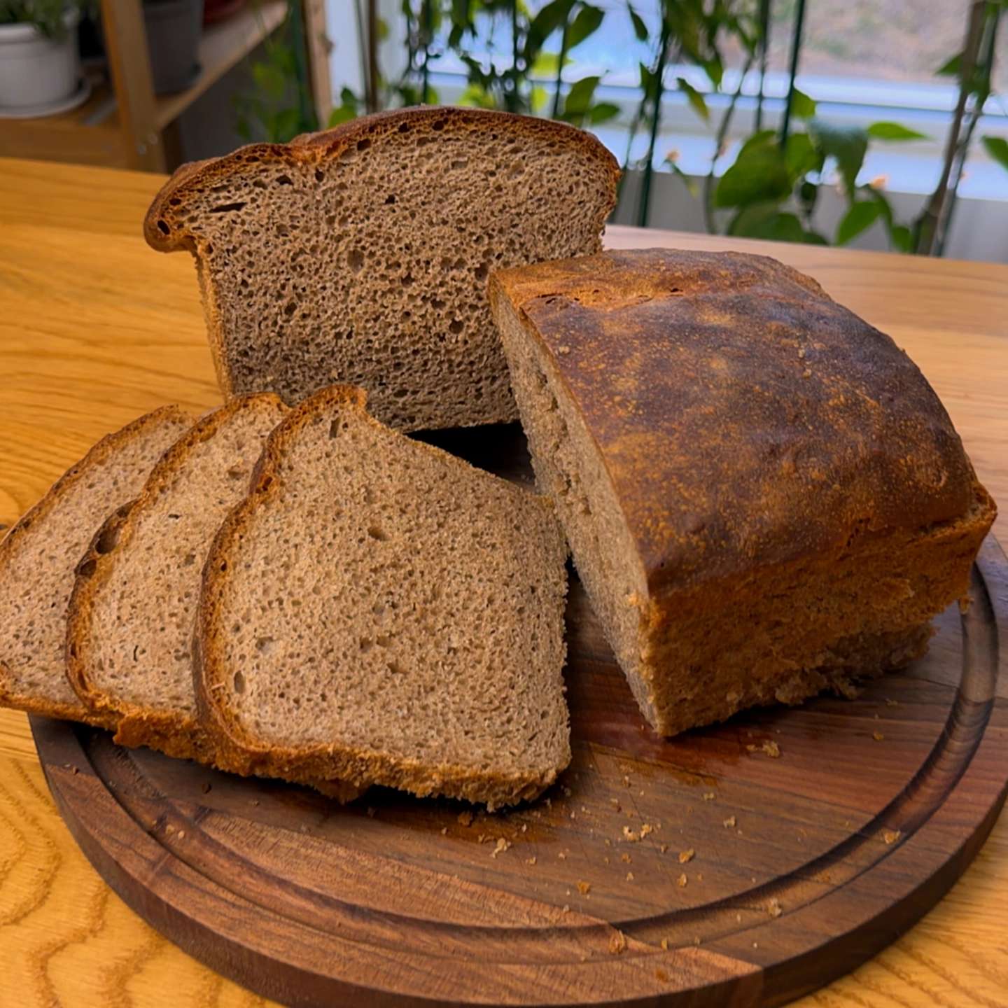 Freshly baked whole wheat loaf of bread, partially sliced on a round wooden cutting board.