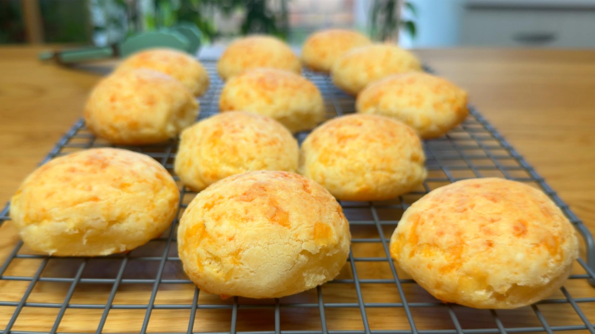 Freshly baked Brazilian cheese bread (Pão de Queijo) cooling on a wire rack, with a golden crust and cheesy texture.