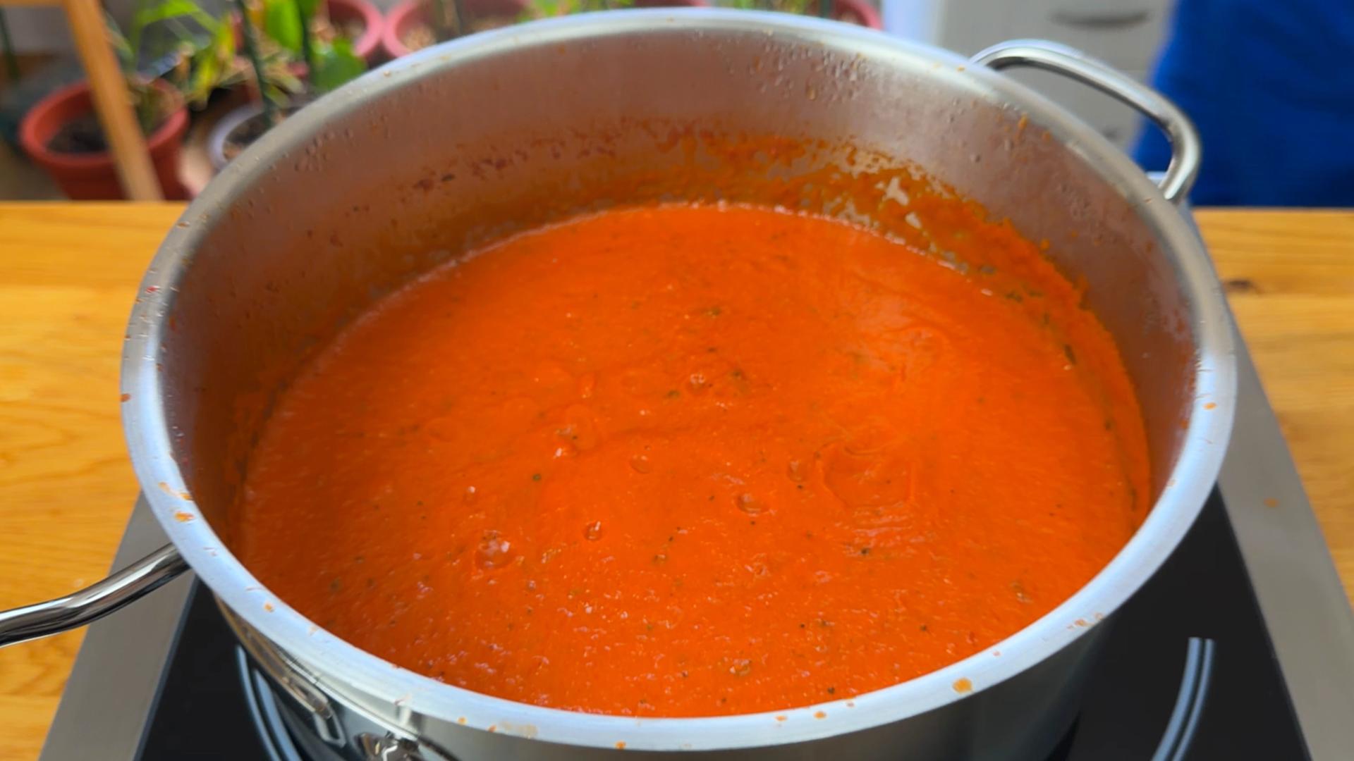 Smooth red marinara sauce simmering in a large stainless steel pot on a stove.