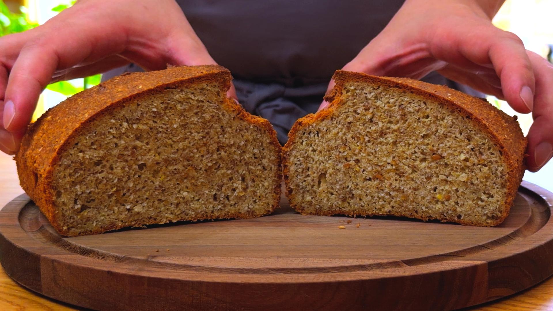 Sesame and flaxseed bread sliced open to show a dense, hearty crumb, displayed on a wooden serving board.