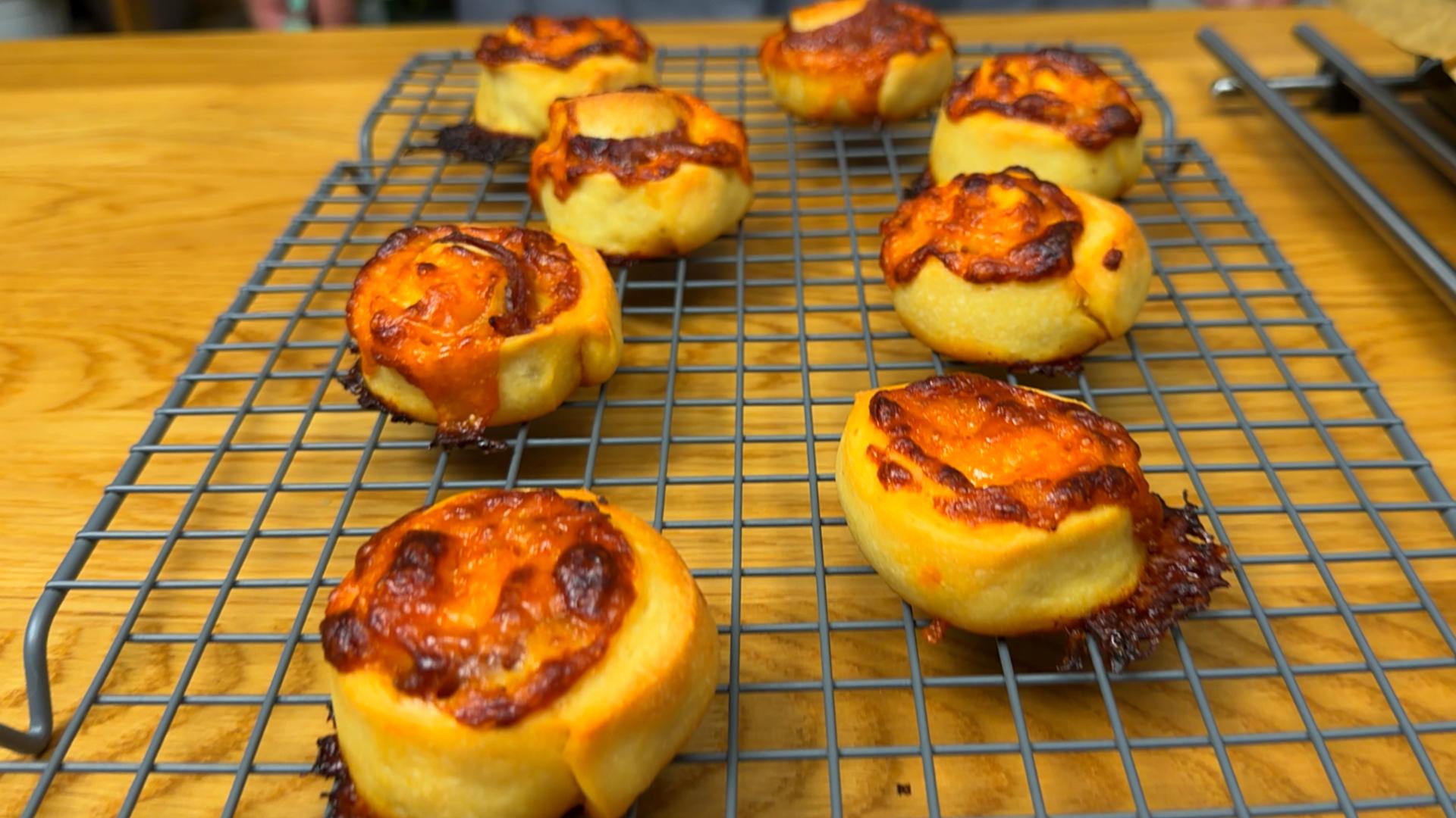Freshly baked cheesy pizza rolls cooling on a metal wire rack on a wooden surface.