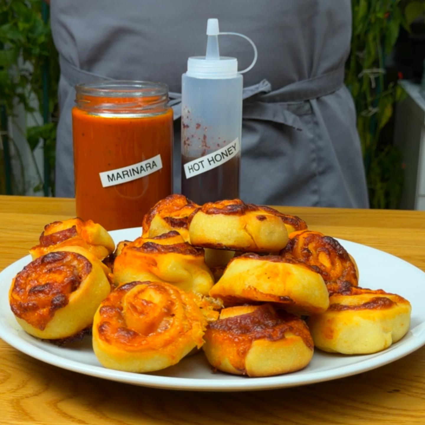 Close-up of a plate of baked pizza pinwheels served with containers of marinara sauce and hot honey.