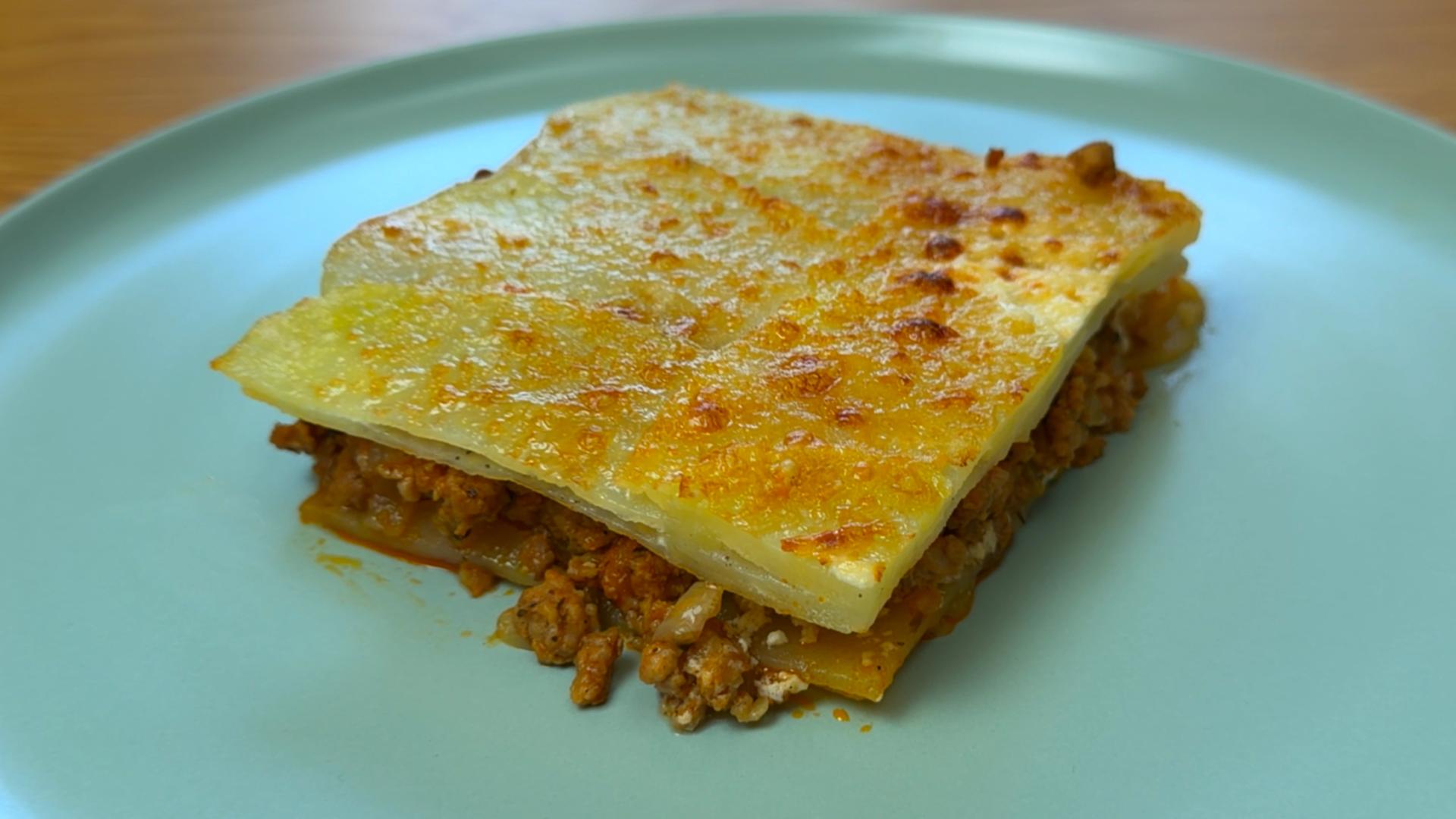A square slice of baked potato and minced meat moussaka on a blue plate.