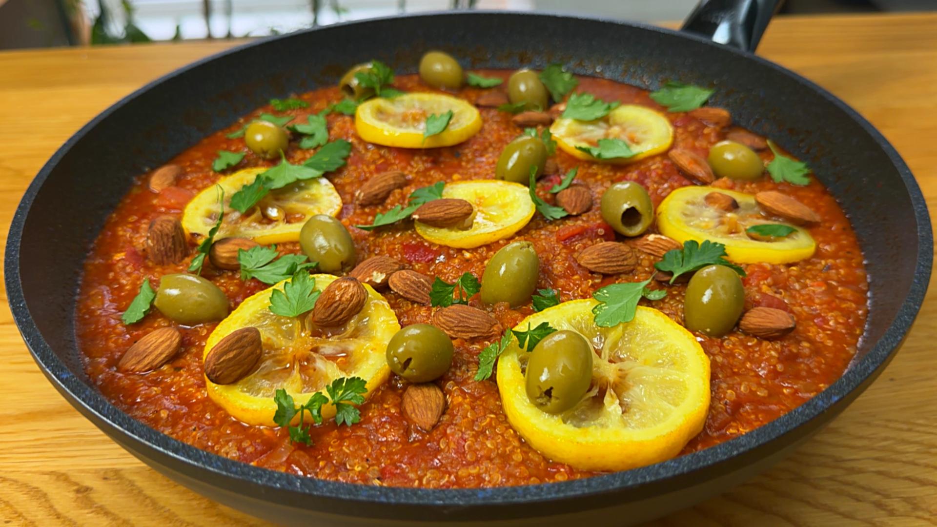 Angled close-up of a completed quinoa harissa skillet topped with lemon wheels, whole almonds, green olives, and parsley.
